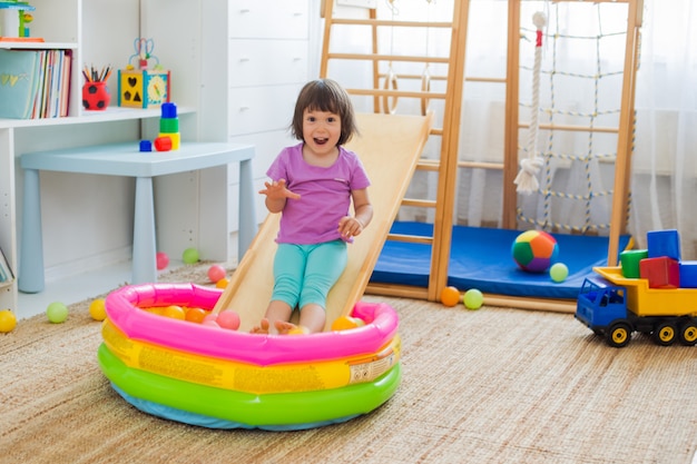 Niña que se divierte montando una montaña rusa en una escalera de complejo de juegos deportivos de casa de madera