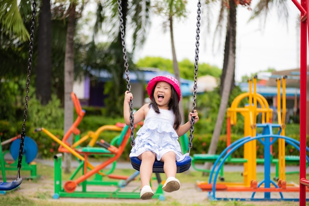 Niña que se divierte con el oscilación en el parque. Patio de los niños.