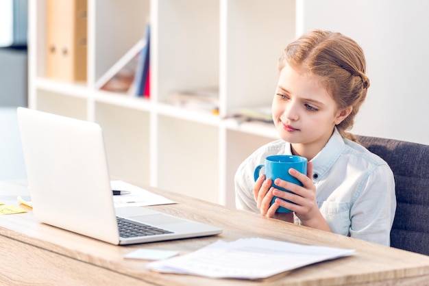 Foto niña que finge ser mujer de negocios y trabaja con una computadora portátil en la oficina