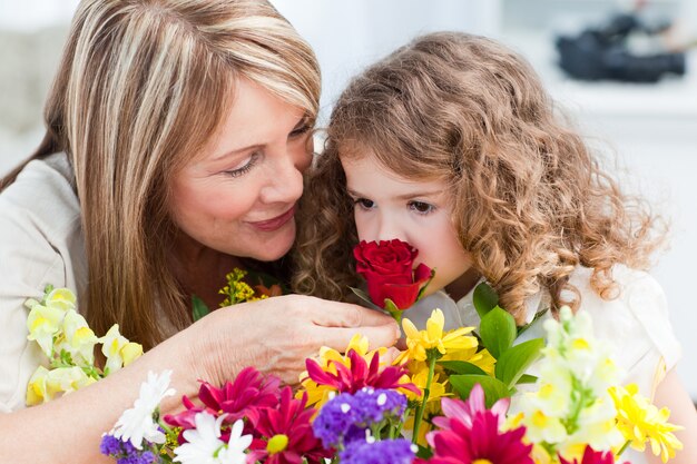 Foto niña que huele flores mientras su abuela está sonriendo