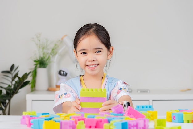 la niña que lleva una camisa brillante está feliz jugando rompecabezas de bloques de colores en la habitación blanca
