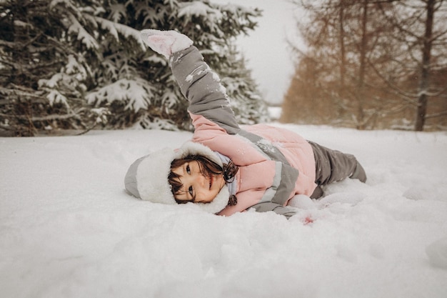 Una niña que se ríe con un cálido traje de invierno yace en la nieve profunda.