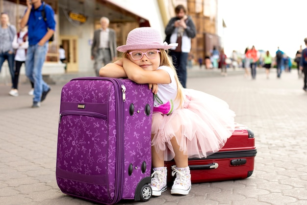 Foto niña que se sienta en una maleta en la estación de tren.