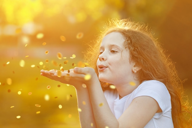 Foto niña que sopla confeti de oro con su mano.