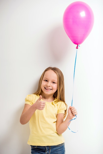 Niña que sostiene el globo rosado y que muestra los pulgares para arriba.