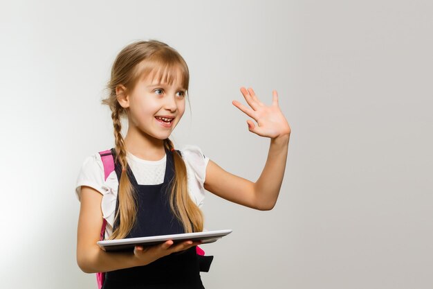 La niña que usa la tableta en el fondo de la pared blanca