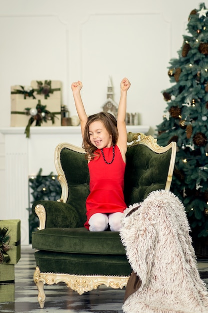 La niña se quedó dormida en la sala de estar en un sillón esperando a Santa la noche de Navidad.