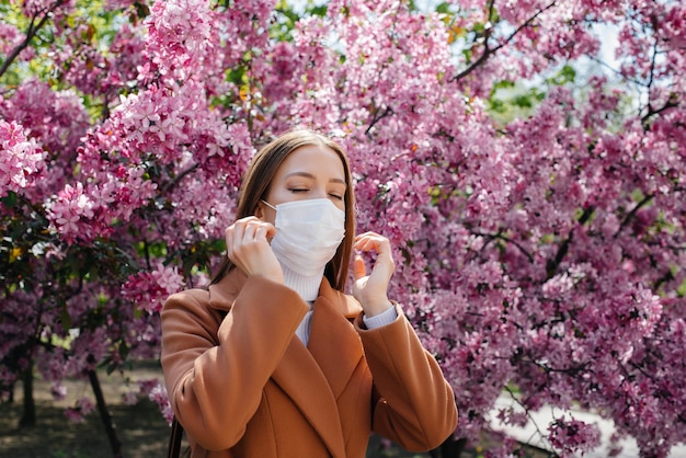 Una niña se quita la máscara y respira profundamente después del final de la pandemia en un día soleado de primavera, frente a jardines floridos. Protección y prevención covid 19.