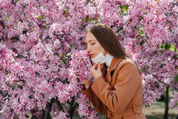 Una niña se quita la máscara y respira profundamente después del final de la pandemia en un soleado día de primavera, frente a los jardines en flor. Protección y prevención covid-19.
