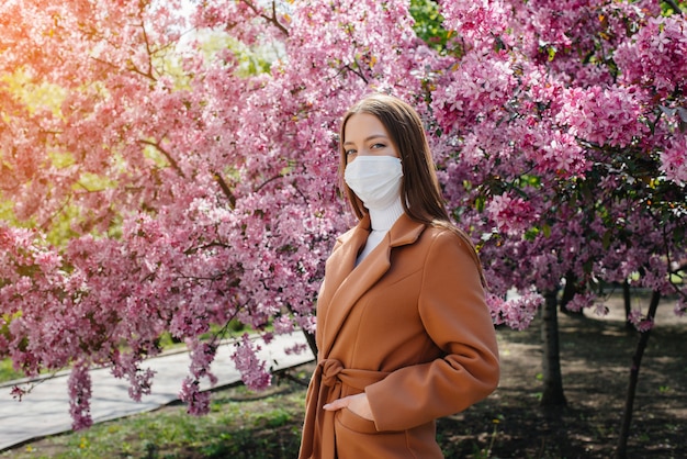Una niña se quita la máscara y respira profundamente después del final de la pandemia en un soleado día de primavera, frente a los jardines en flor. Protección y prevención covid 19.