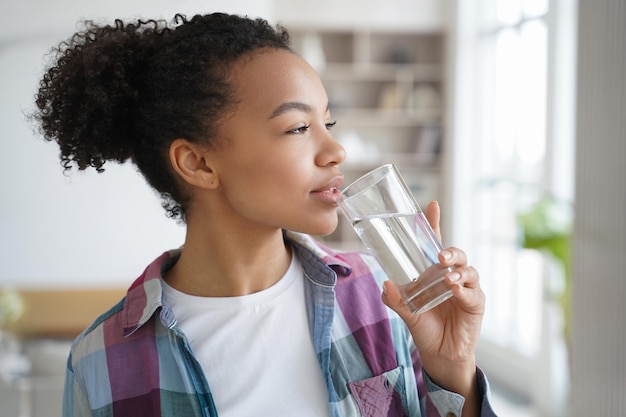 Niña de raza mixta bebe agua pura de vidrio en casa Rutina matutina de estilo de vida saludable