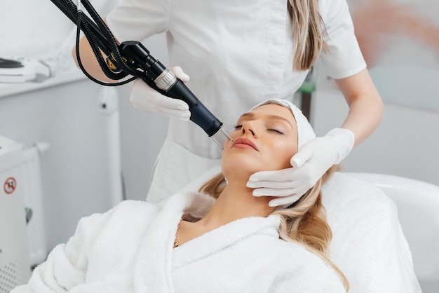 Una niña recibe un peeling de carbón para la piel de la cara en un salón de belleza Los pulsos de láser limpian la piel Cosmetología de hardware El proceso de fototermólisis que calienta la piel