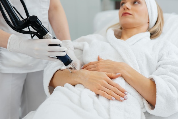 Una niña recibe un peeling de carbón para la piel de sus manos en un salón de belleza Los pulsos de láser limpian la piel Cosmetología de hardware El proceso de fototermólisis que calienta la piel