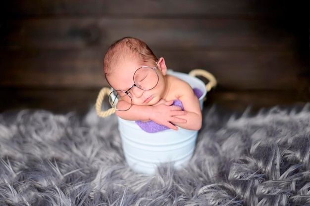 Una niña recién nacida dentro de un cubo de metal blanco y con gafas enormes