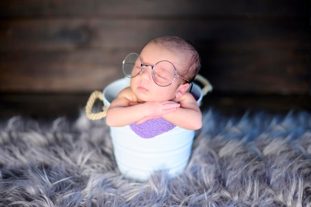 Una niña recién nacida dentro de un cubo de metal blanco y con gafas enormes