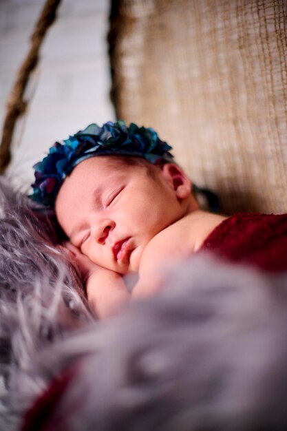 Una niña recién nacida durmiendo en un lazo de tela con una diadema de flores azules