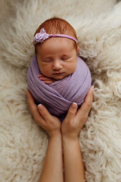 La niña recién nacida está durmiendo en una postura de capullo (bolsa de papa) en los brazos de su madre. El concepto de seguridad y felicidad.