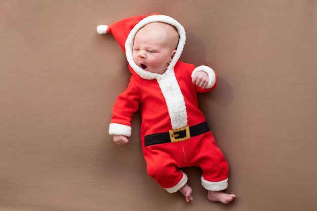 Niña recién nacida vestida con traje de santa claus bostezando cansada Año Nuevo o concepto de Navidad