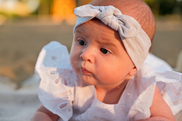 La niña recién nacida yace en la playa con un vestido blanco