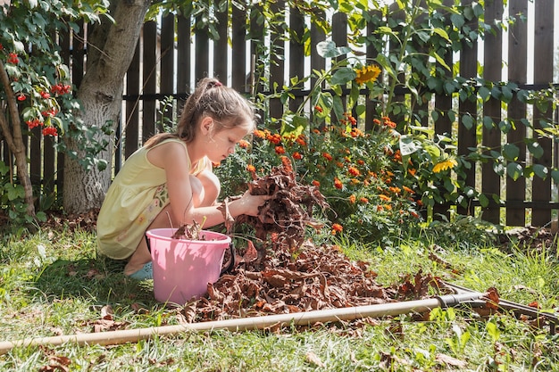 Niña recoge hojas secas en un balde en el jardín