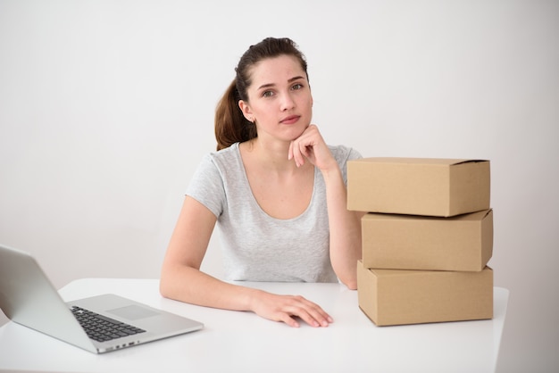 La niña recoge los pedidos en cajas de cartón. Cerca hay una pila de paquetes sobre la mesa. Concepto - servicio de entrega.