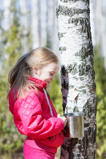 Niña recoge savia de abedul en el bosque