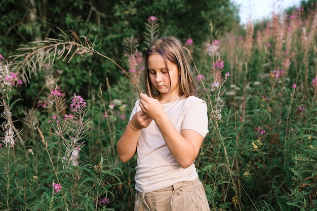 Niña recogiendo flores silvestres a la luz del atardecer, caminando en el prado de verano. Momento auténtico atmosférico. Mano recogiendo flores en el campo. Vida rural lenta