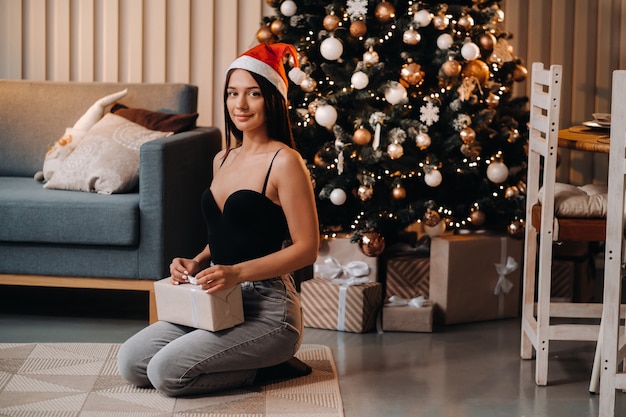 Una niña con un regalo de año nuevo en sus manos está sentada en su casa cerca del árbol de Navidad