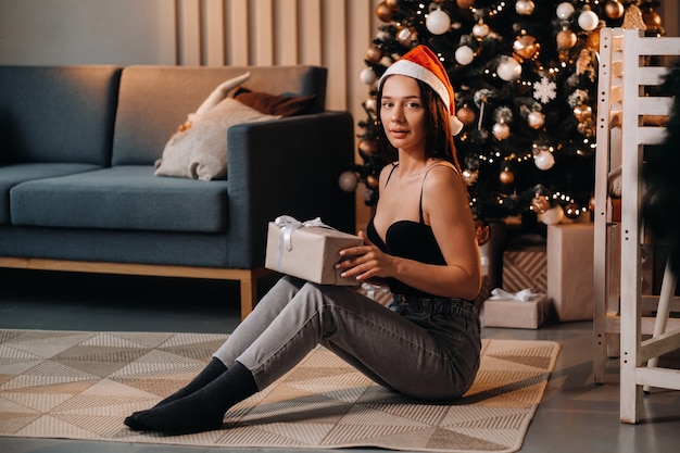 Una niña con un regalo de año nuevo en sus manos está sentada en su casa cerca del árbol de Navidad