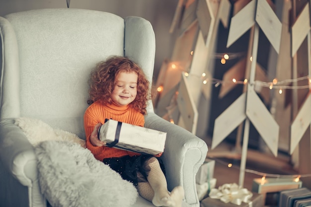 Niña con un regalo de Navidad sentado en una silla cómoda