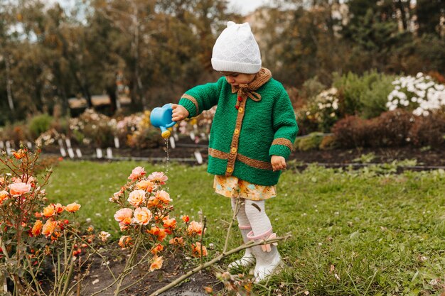 Niña regando flores con una regadera en el jardín