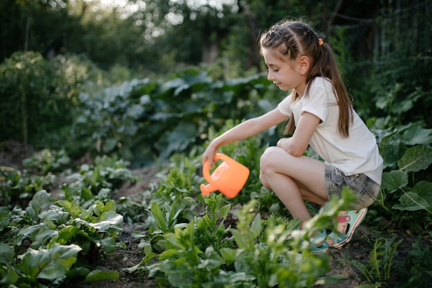 Niña regando el jardín en verano por la mañana