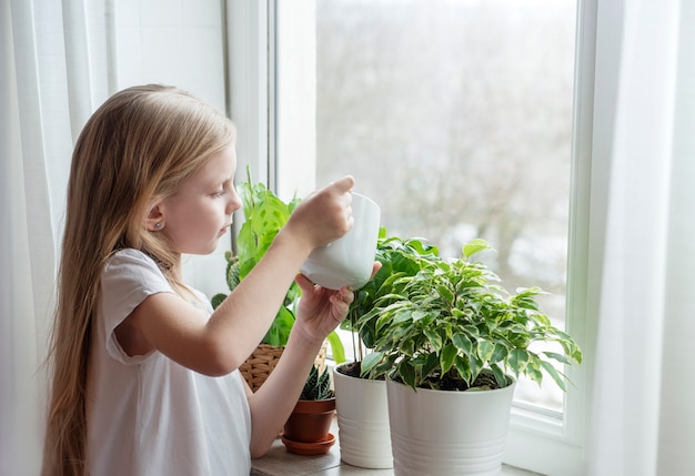 Niña regando plantas de interior en su casa