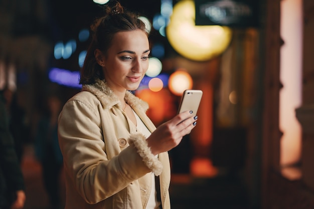 Foto niña revisando su teléfono afuera en la noche