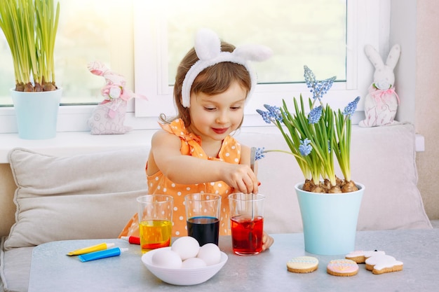 Foto la niña revuelve la solución coloreada para pintar los huevos para las vacaciones de semana santa.