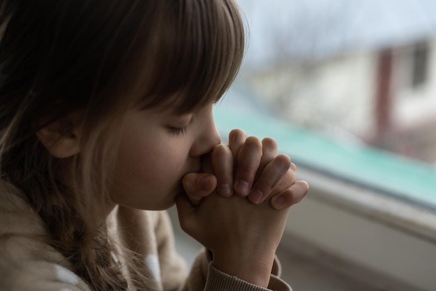 Niña rezando cerca de la ventana