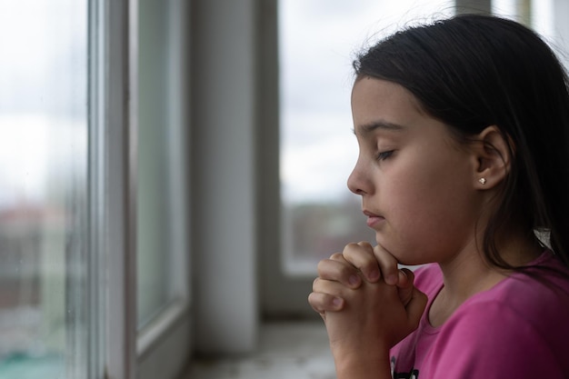 Niña rezando en la mesa blanca por la mañana. Mano de niña rezando, manos dobladas en concepto de oración por la fe, la espiritualidad y la religión.