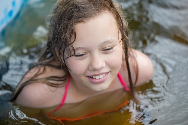 La niña se ríe en la piscina en el día de verano.