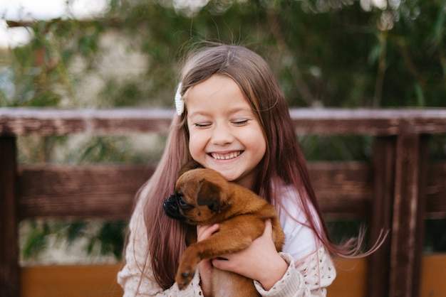 Niña se ríe y sostiene un pequeño perro marrón en sus brazos