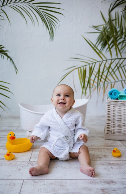 Una niña riendo en bata de baño está sentada cerca de una bañera para bebés.  higiene infantil