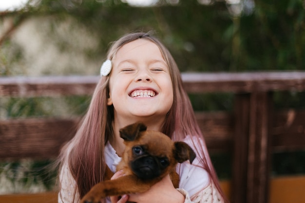 Niña riendo sosteniendo un pequeño perro marrón en sus brazos