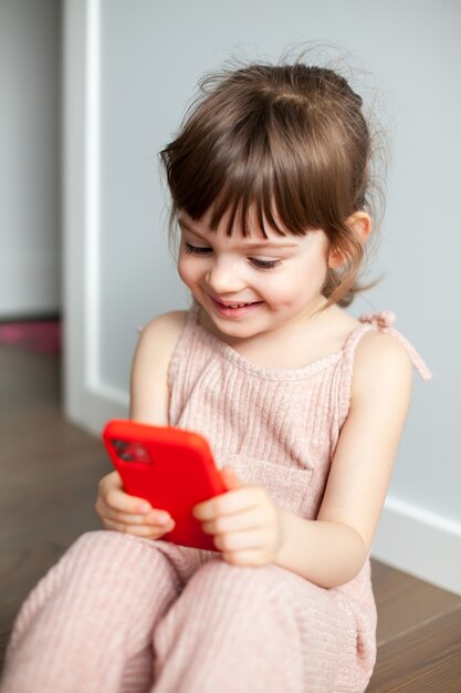 Niña riendo con teléfono móvil sentado en el suelo. Ella está jugando o viendo dibujos animados en su teléfono inteligente. Concepto de adicción al teléfono y generación digital.