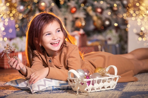 Una niña riendo yace en el suelo con decoración navideña en sus manos