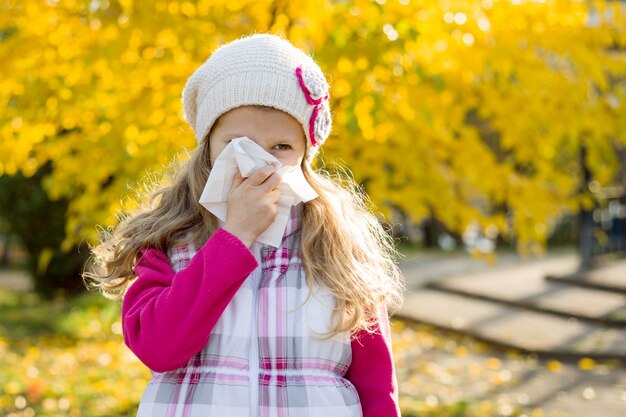 Niña con rinitis fría sobre fondo de otoño