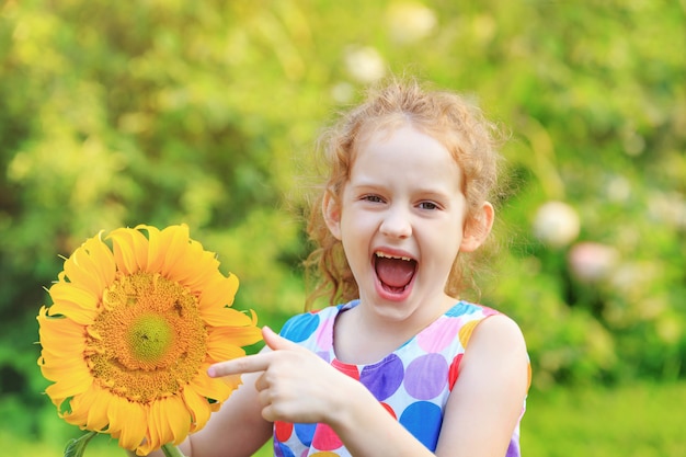 La niña de risa sostiene el girasol.