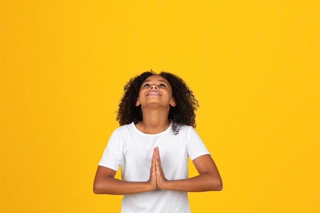 Niña rizada adolescente sonriente en camiseta blanca mirando hacia arriba gesto de oración