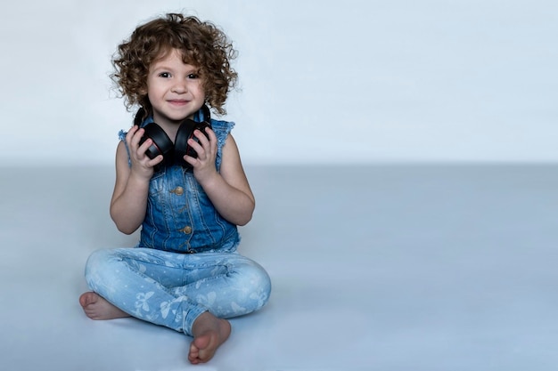 Foto niña rizada sentada en el suelo con auriculares negros