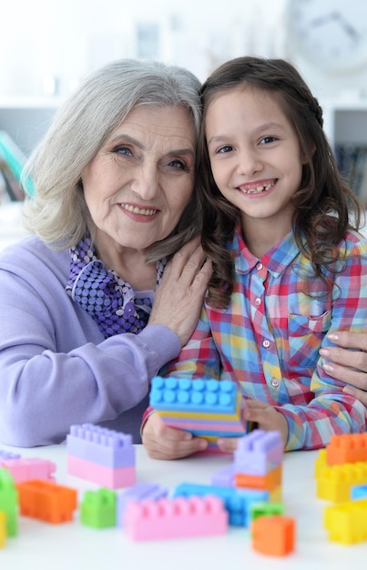 Niña rizada y su abuela jugando con coloridos bloques de plástico