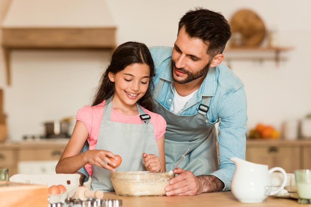 Niña rompiendo huevos con la ayuda de su padre