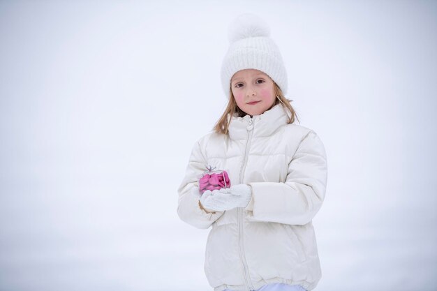 Foto una niña con ropa blanca de invierno en la nieve sosteniendo una caja transparente con dulces en forma de corazones